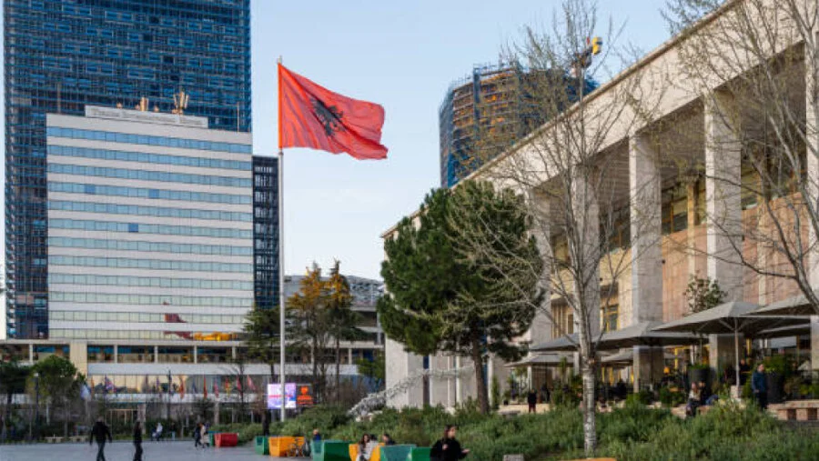 The Albanian flag in front of a colourful government building.