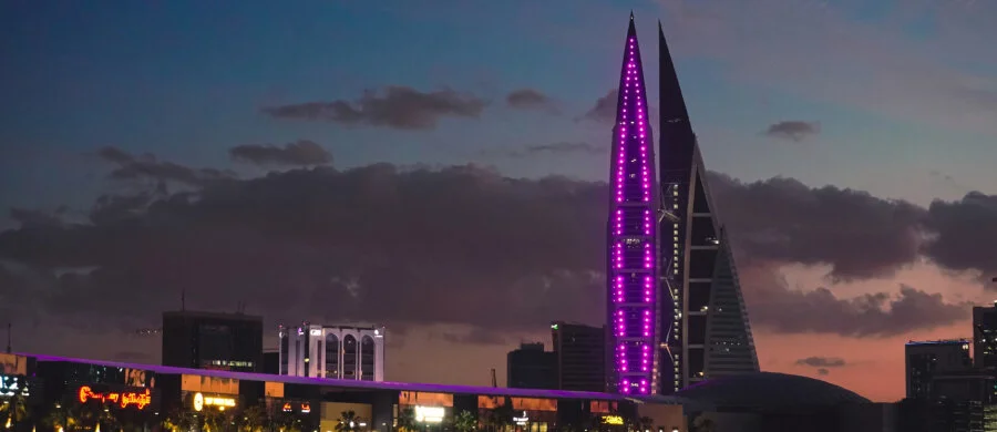 An illuminated waterfront tower, bridges and the Bahrain skyline at dusk.