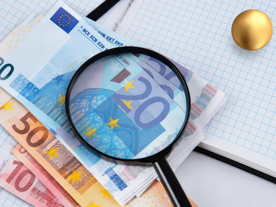 Euro banknotes and accounting documents viewed through a magnifying glass.